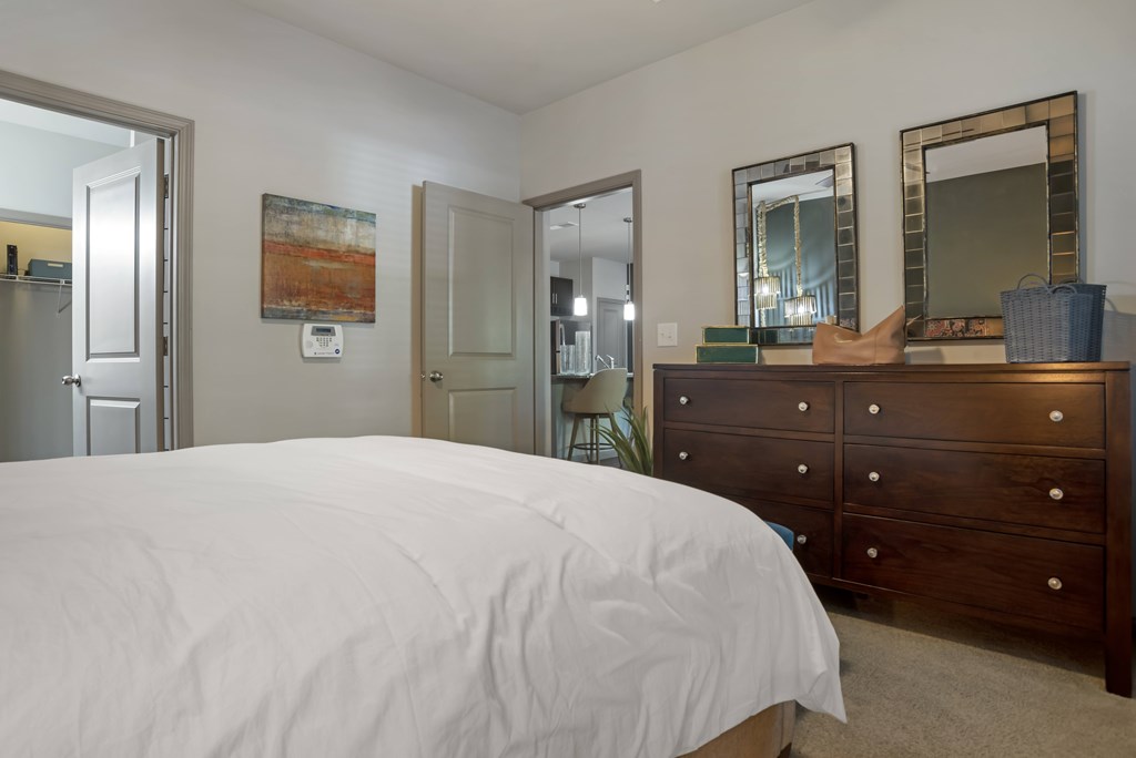 A bedroom with a white bed and a wooden dresser.